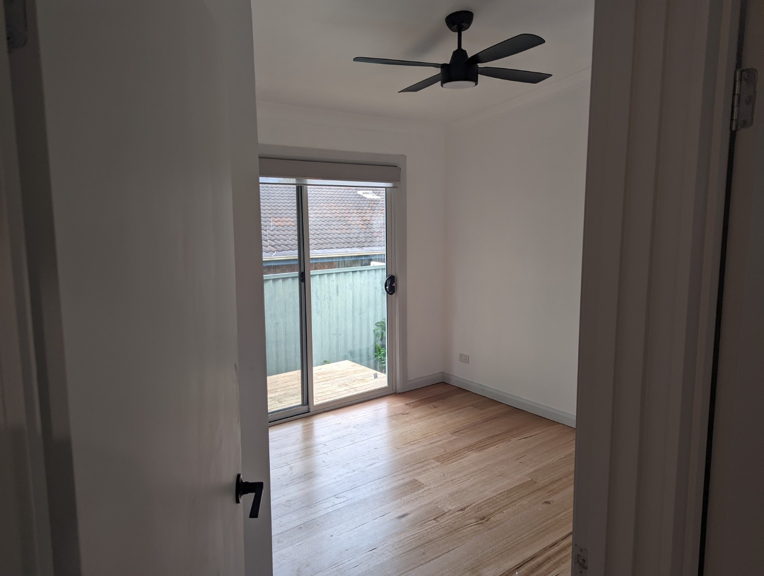 East Gosford granny flat — Bedroom with timber-look flooring, black ceiling fan and sliding door