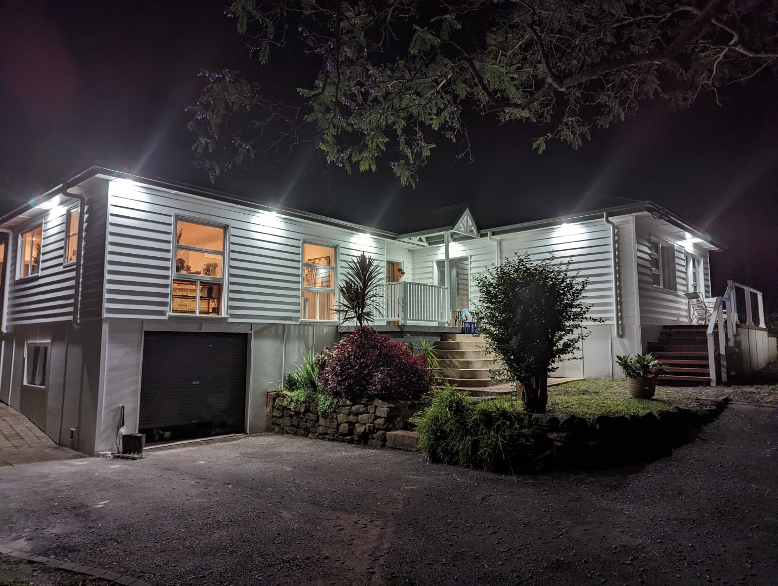 Holgate home at night with white weatherboard cladding, exterior lighting and entry stairs